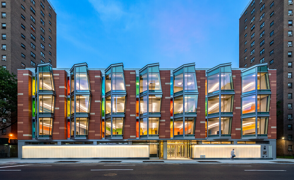 brightly colored glass highlights the extruded window bays and terracotta of the facade at dusk