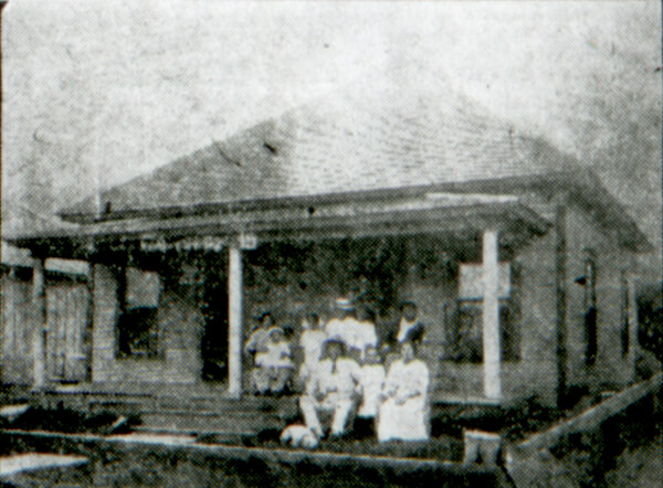 Black and white photo of a family sitting outside of a home