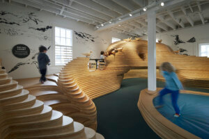 kids frolic on a wooden play structure inside the new Bay Area Discovery Museum space
