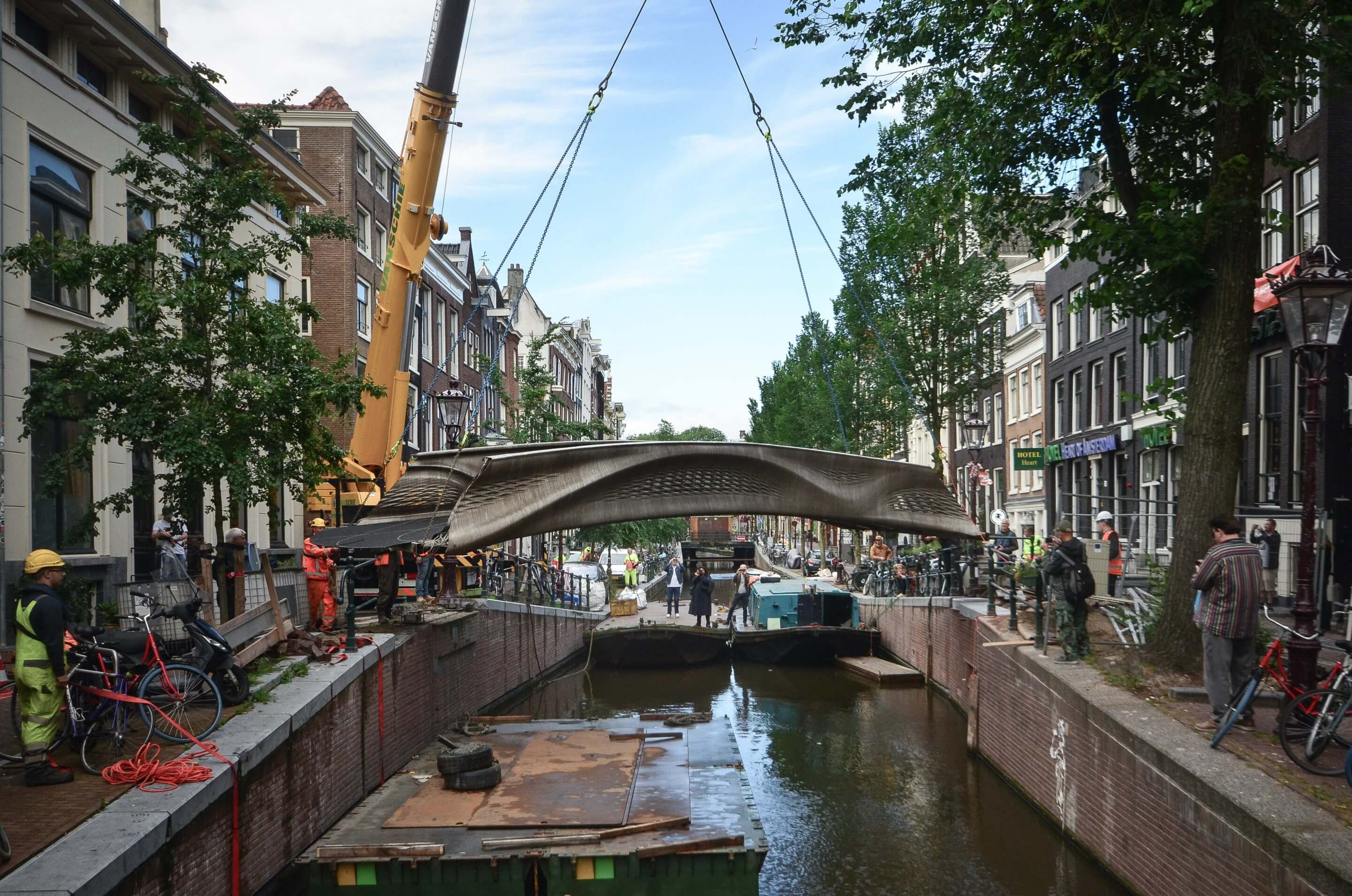 a steel foot bridge being installed by crane over a canal