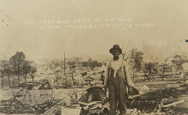 Sepia photo of a man in front of a destroyed house