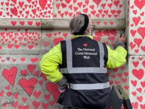 a worker adds a heart to a covid memorial wall
