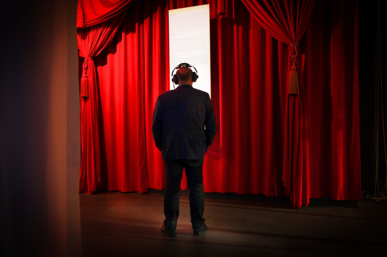 a man wearing headphones stands before a parted red curtain