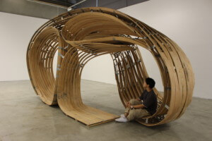 A swirling bent timber pavilion in a white-walled gallery