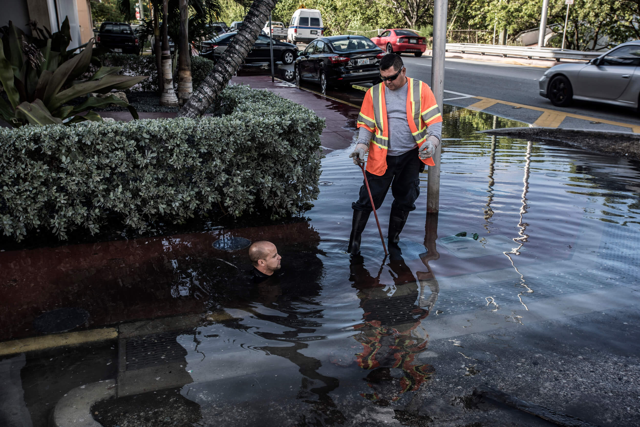 Image of rising waters through drainage system in Miami as a man crouches in drain