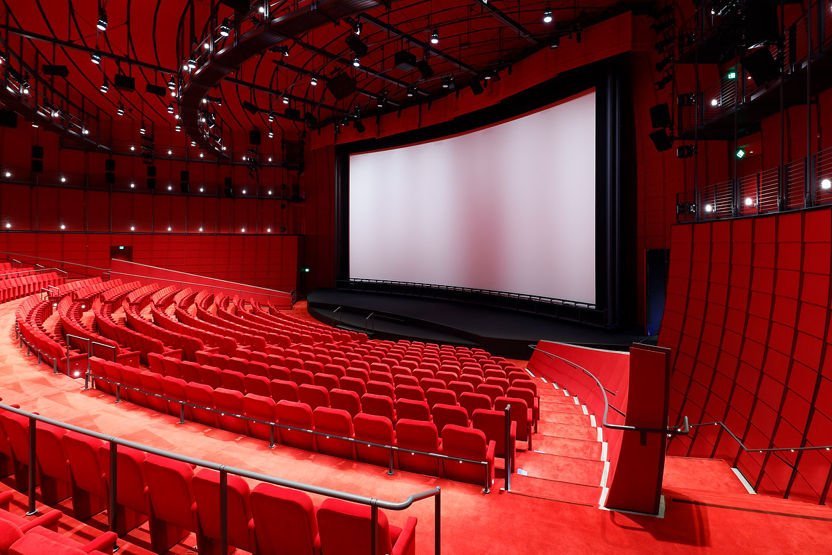 photograph depicting a movie theater with red carpeting, red seats, and red walls