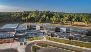 aerial view of a solar panel-topped elementary school campus, forest edge elementart