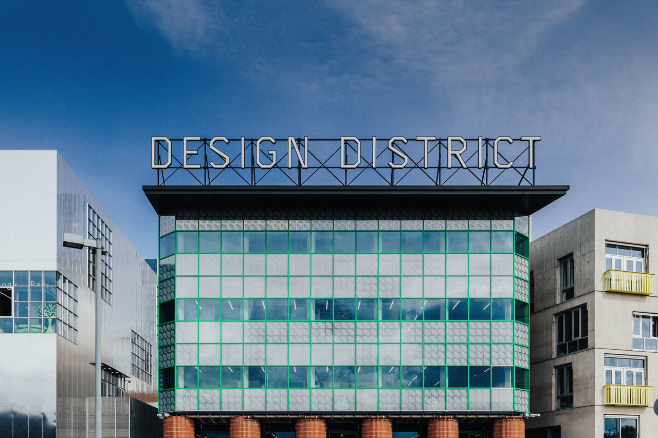 a glass building supported by red pillars with a Greenwich design district sign on top
