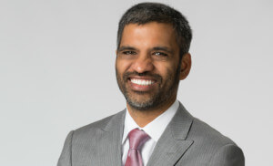 headshot of Mahesh Ramanujam, an indian man in a grey suit