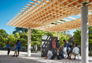 students congregate under a timber pavilion, SPLAM, with a lattice topper prototypical in wood framing