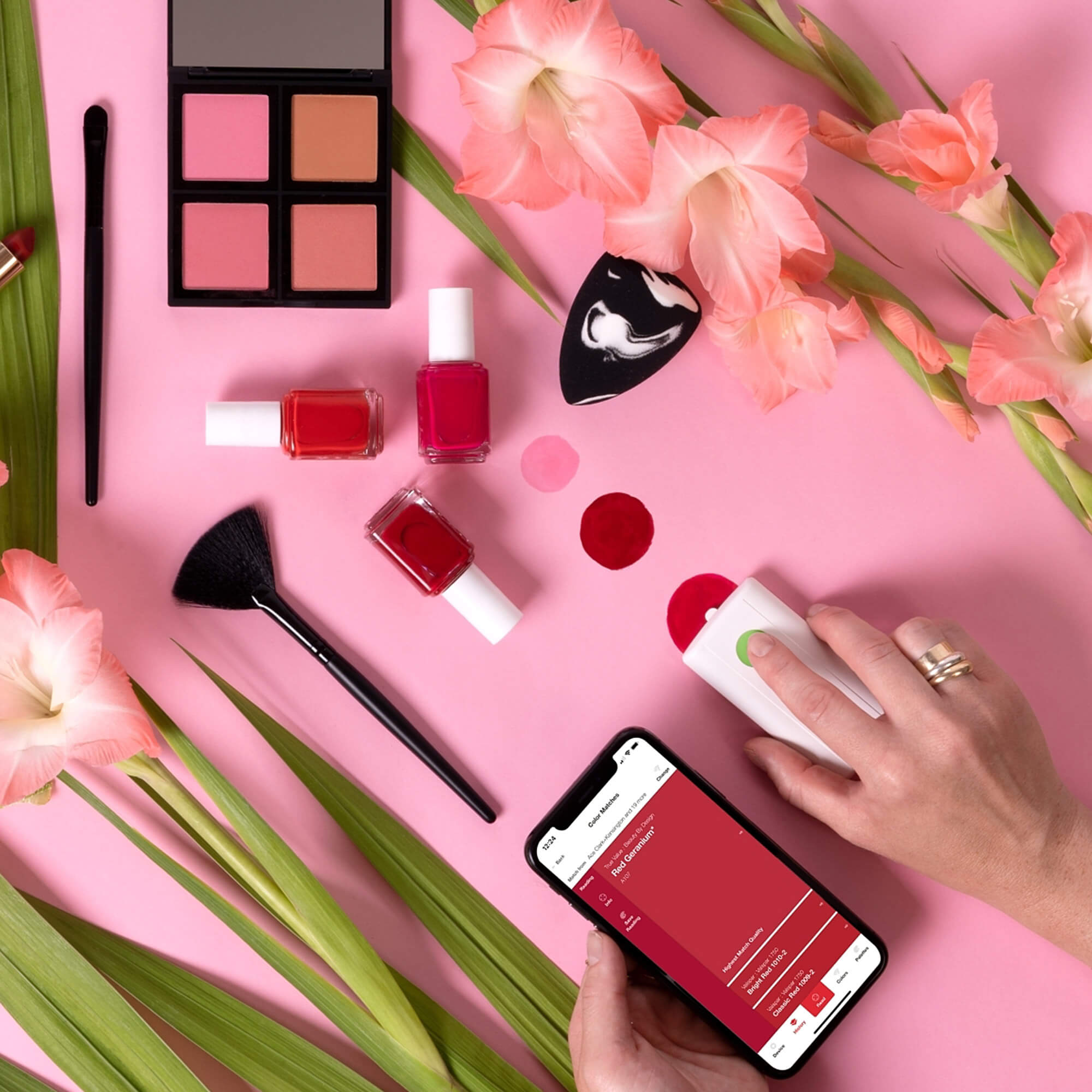 makeup, nail polish, flowers, a brush, human hand, and smartphone on a pink background