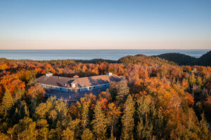 aerial view of a building enveloped by trees with a lake in the distance, the MAC Lodge at the Wolf Ridge Environmental Learning Center in Minnesota