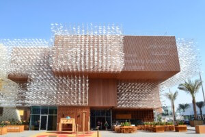 a boxy wooden building clad in a bird-like kinetic sculptural installation, the polish pavilion