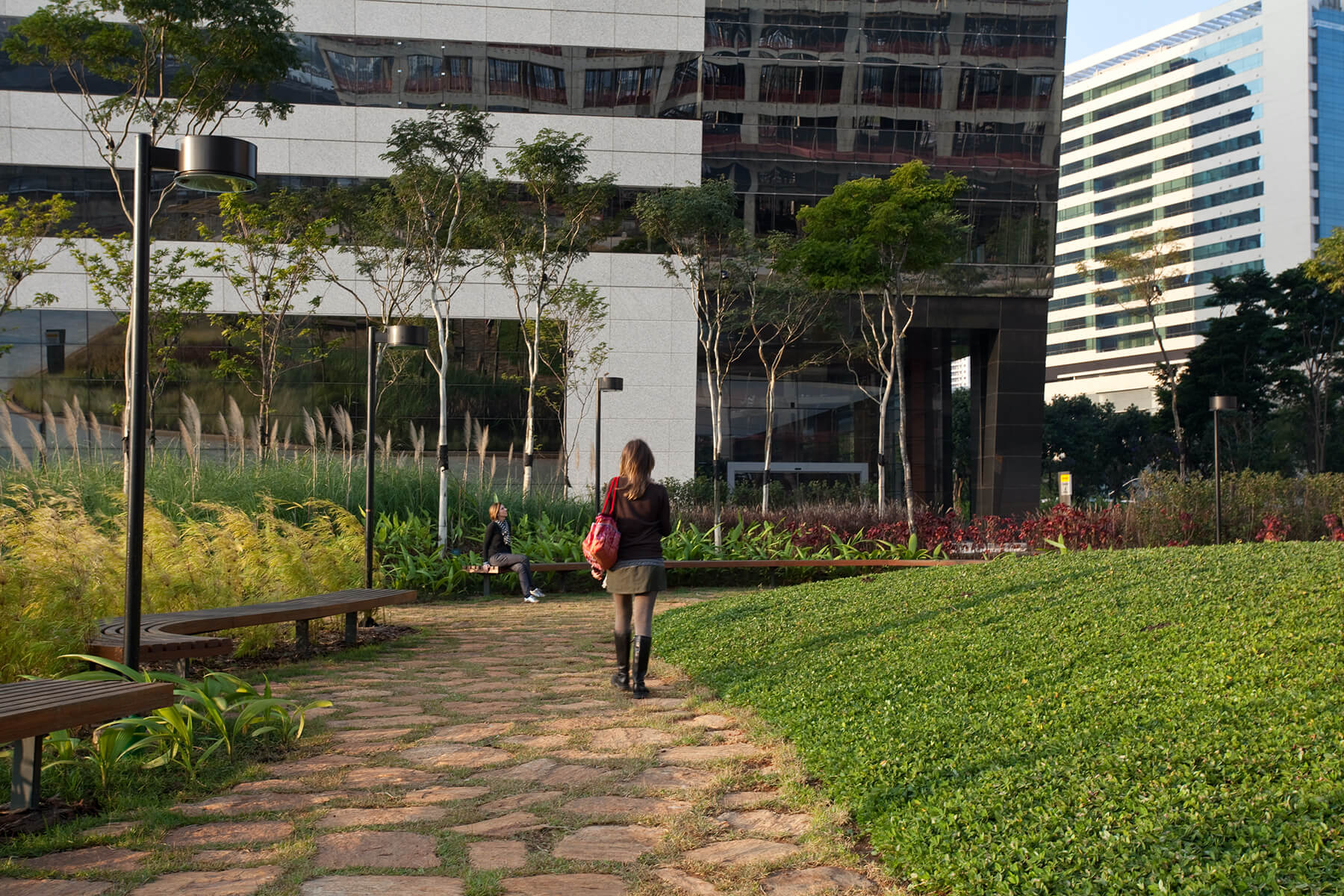a woman walks through a landscaped corporate park surrounded by office towers