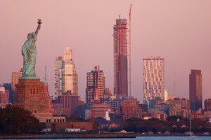 view of a tall, slender skyscraper with the statue of liberty in the foreground