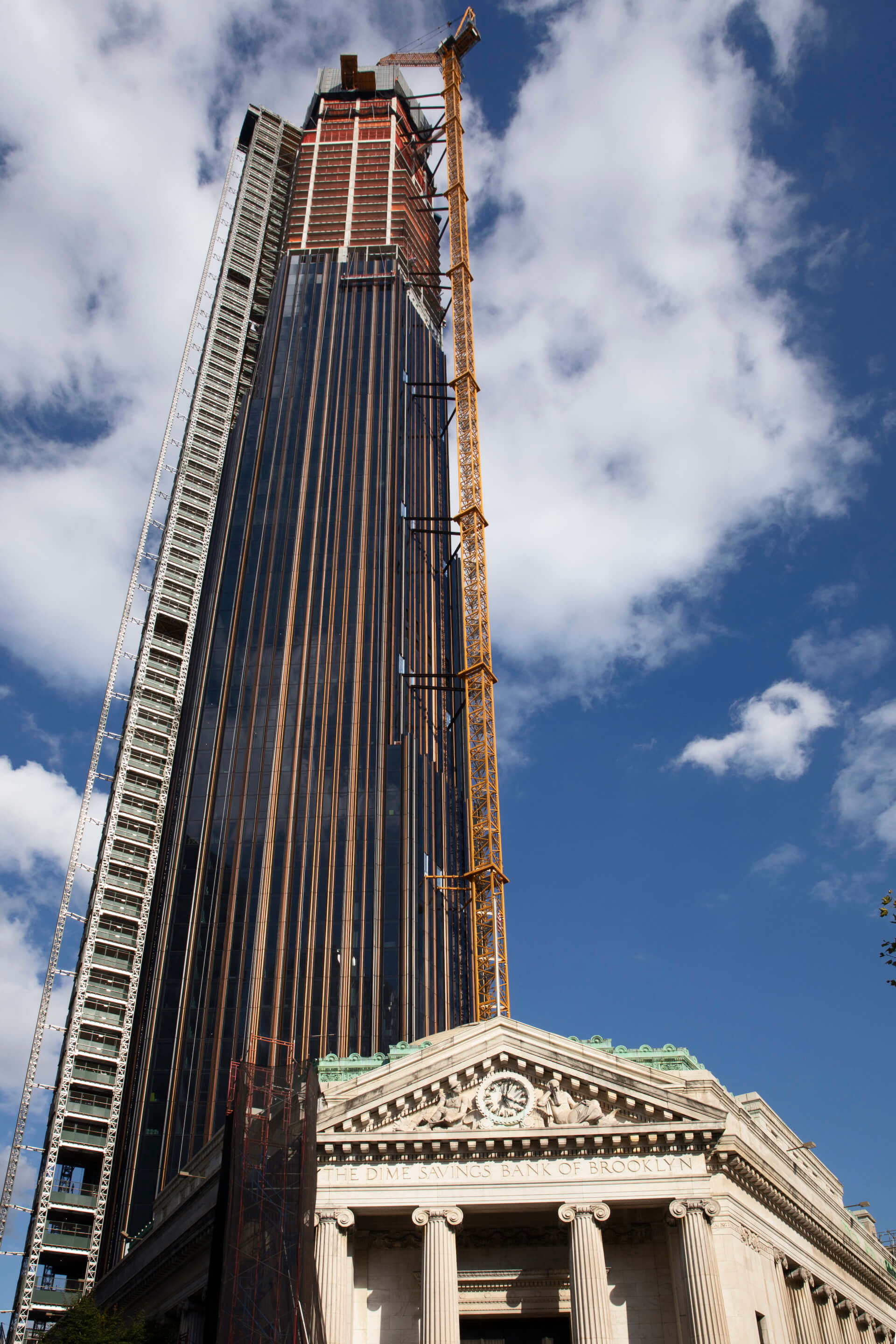 an under-construction supertall tower with a historic bank building in the foreground 