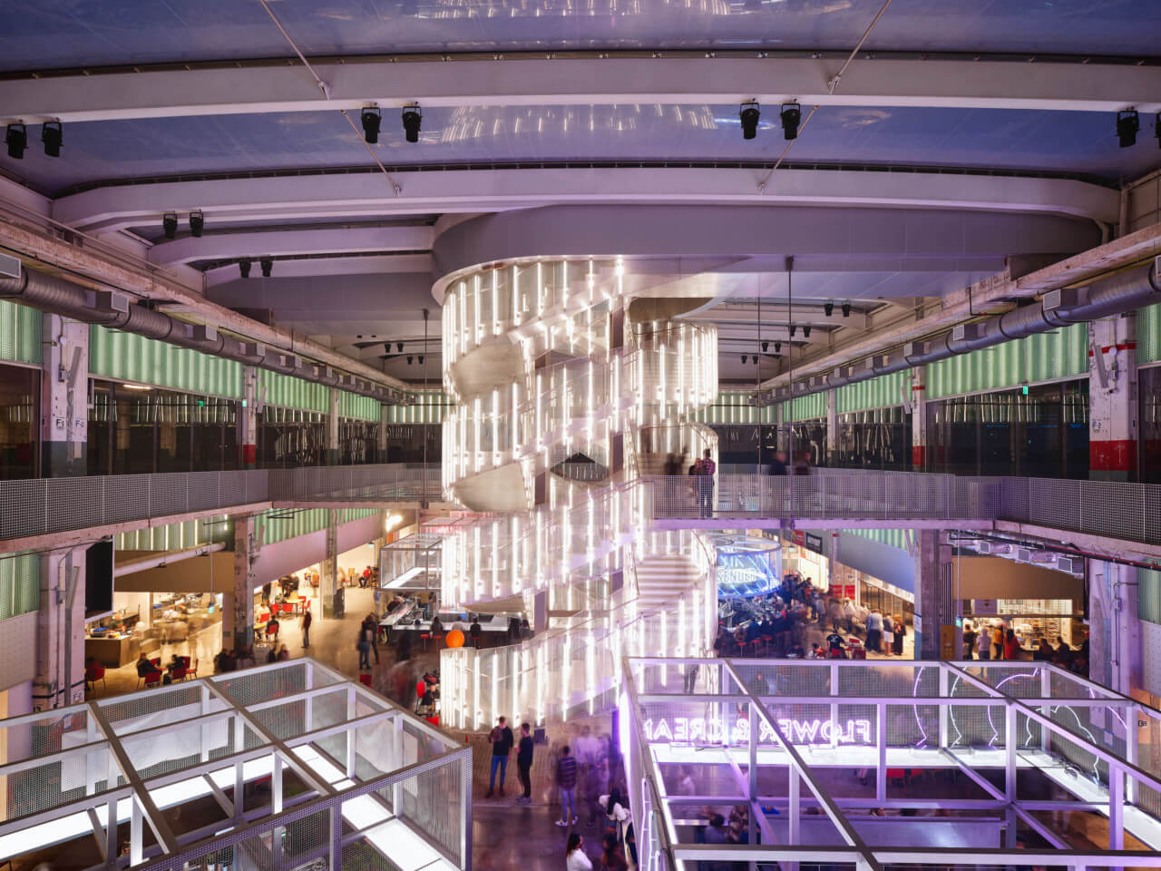 a bustling public atrium illuminated in purple hues with a spiraling staircase at its center