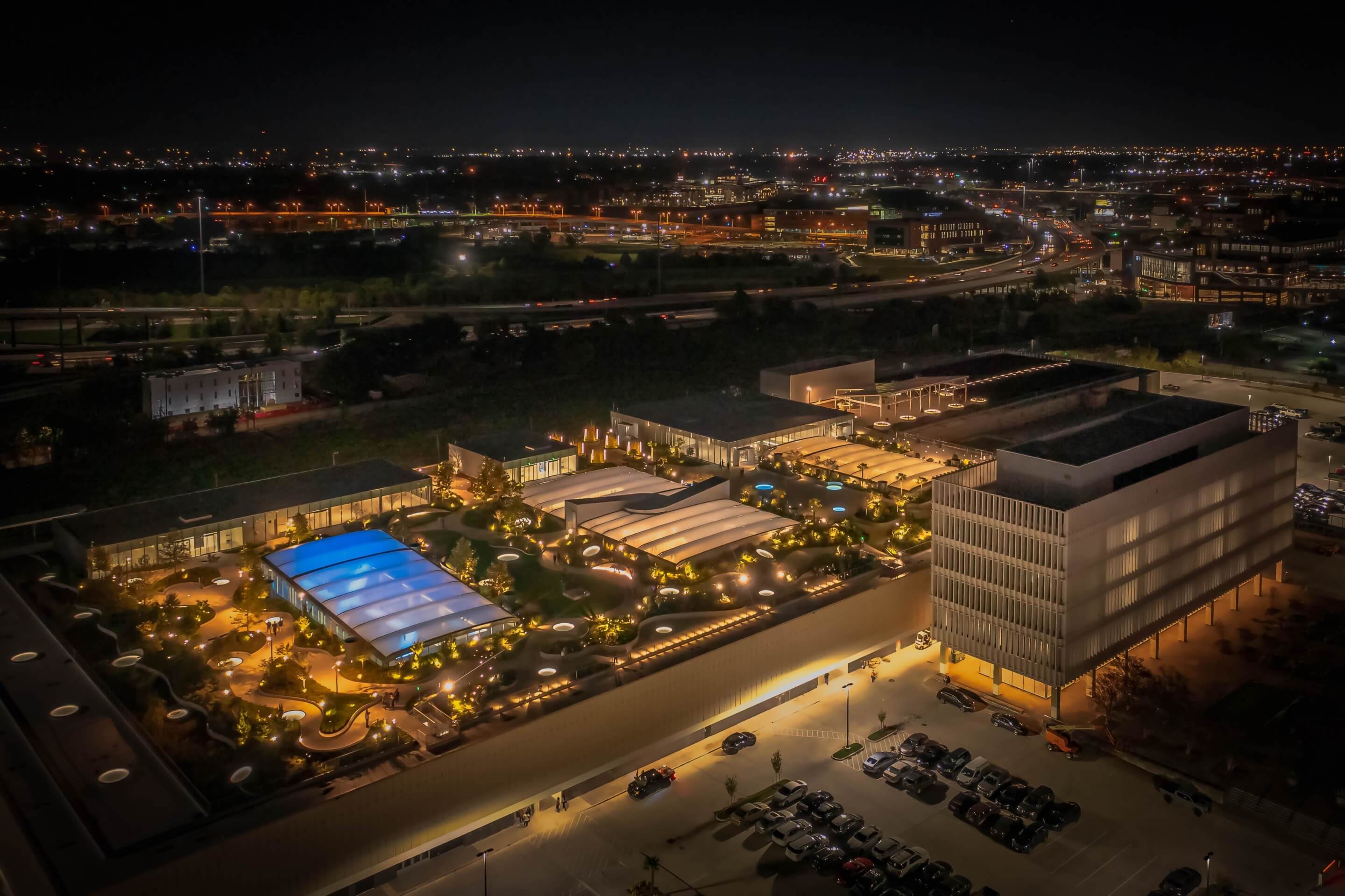 aerial nighttime view of a low-slung mixed-use complex with a large rooftop park