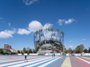 a bowl-shaped mirrored building with trees on top