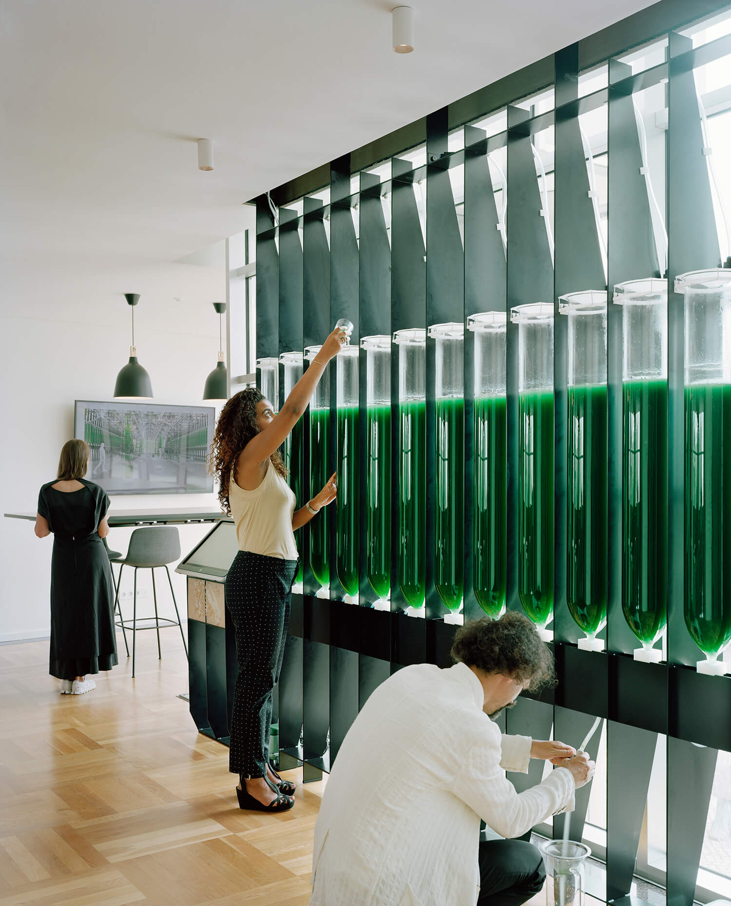 A row of green tubes with someone pouring in the top and another person filtering at the bottom