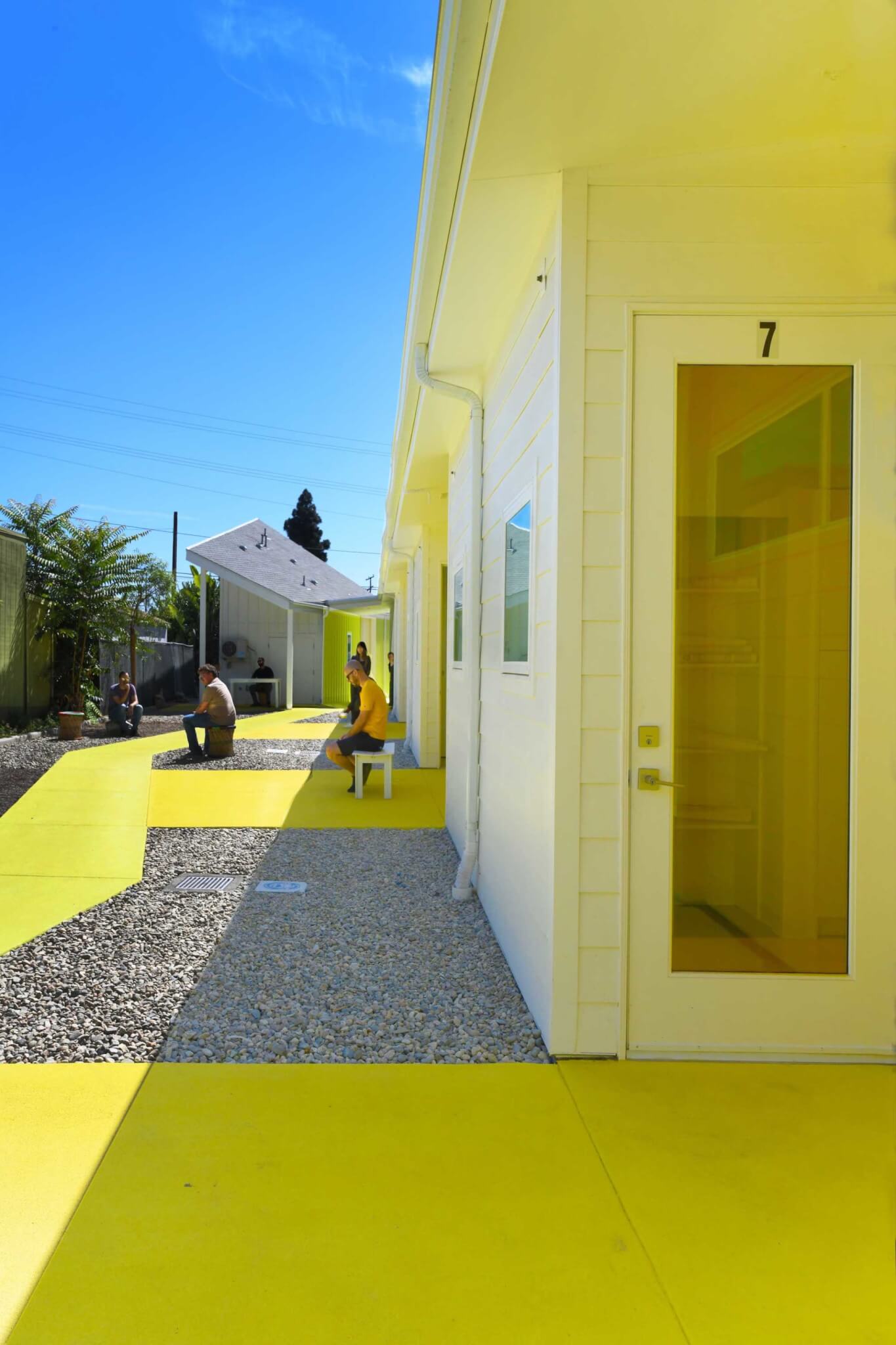 people sit outside housing units on yellow-painted communal spaces