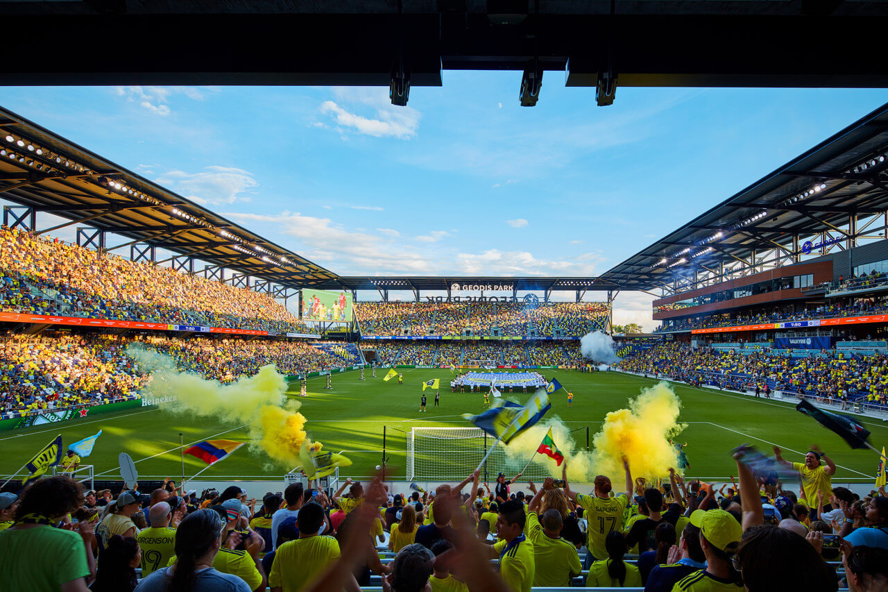 fans watch a soccer match with yellow smoke on the field