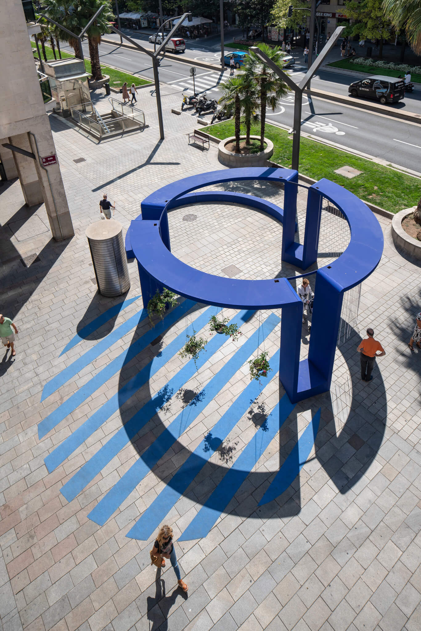 people walk around a large circular blue pavilion in an urban space