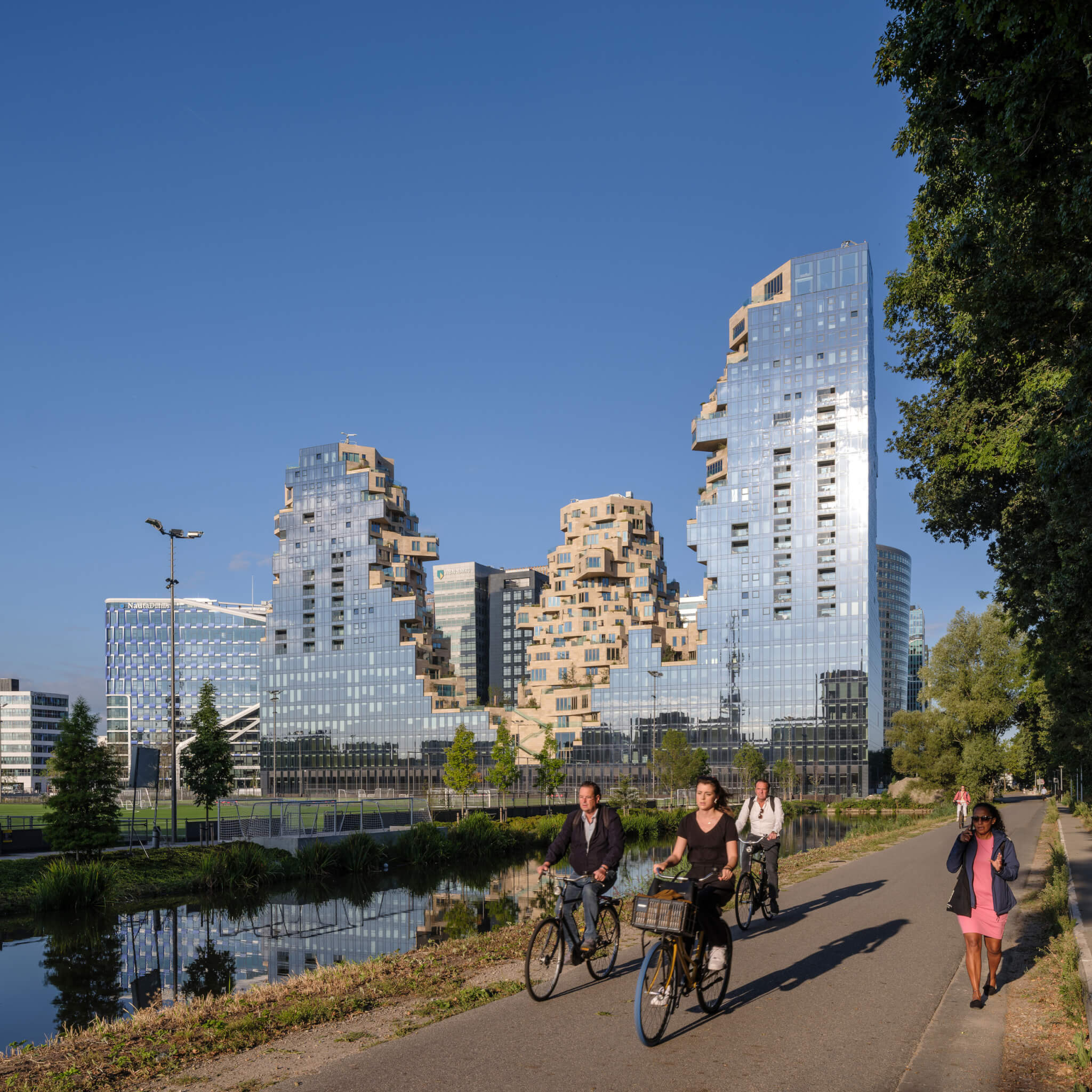 people bike near jagged towers clad in reflective glass