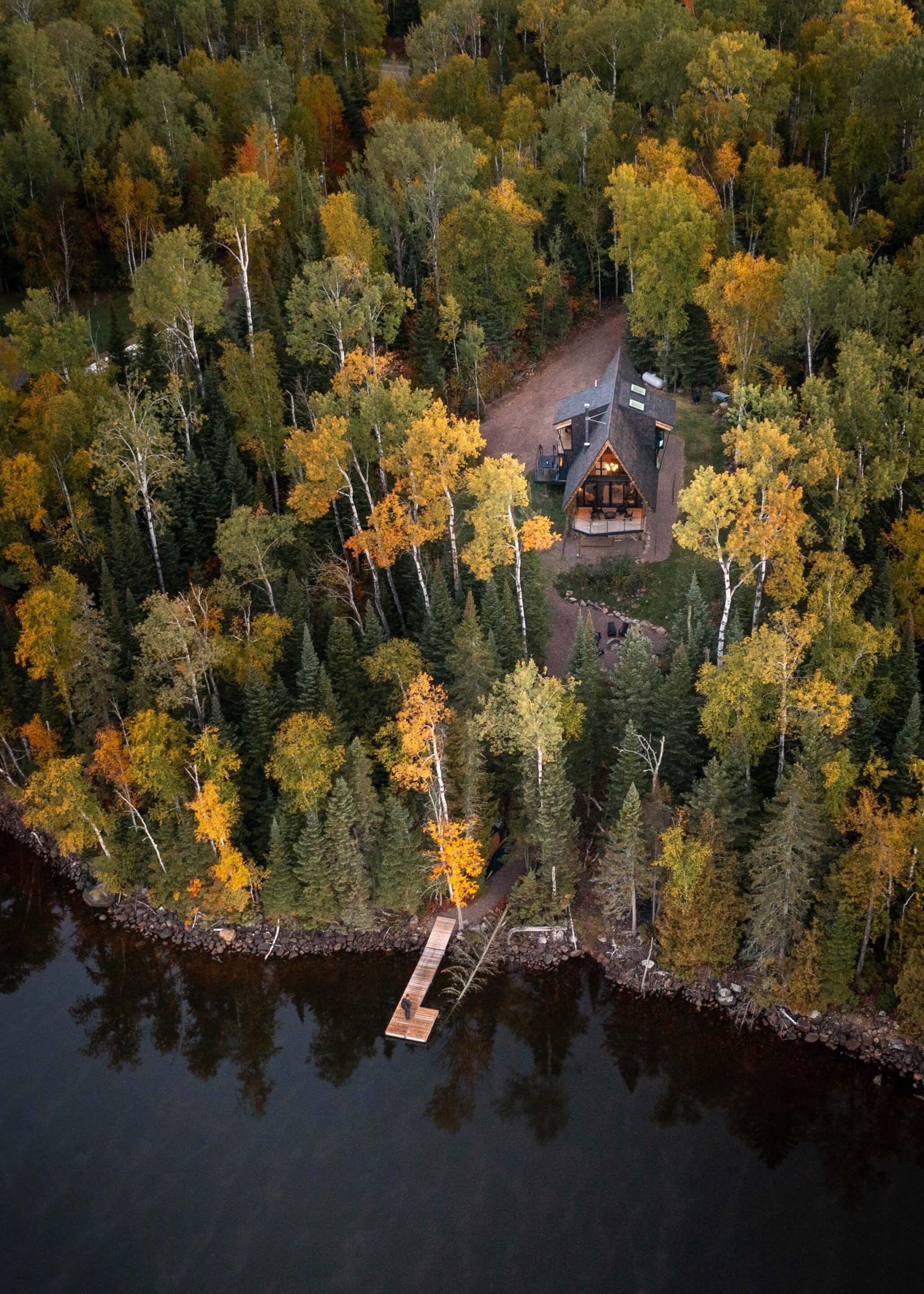 aerial view of a cabin surrounded by trees overlooking a lake