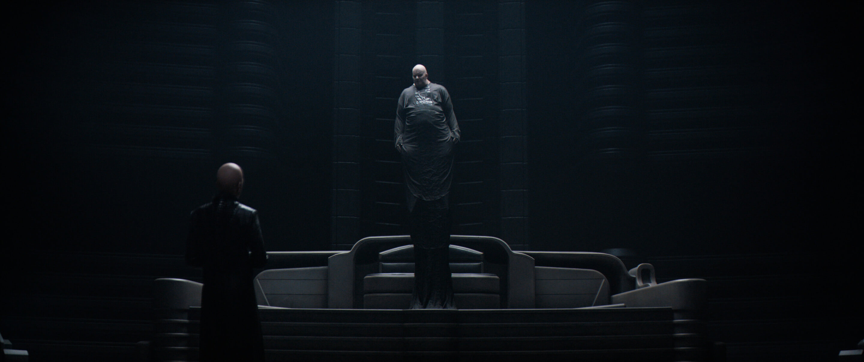 A bald man floating toward the ceiling in a ribbed black room