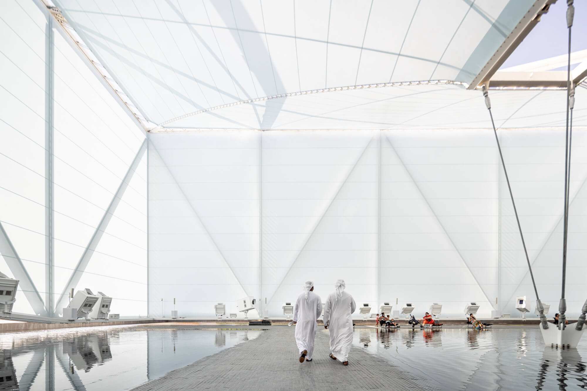 people walk across a shallow pool of water in a white fabric-sheathed structure