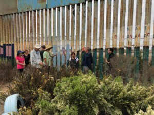 people stand along a fence straddling the u.s.-mexico border