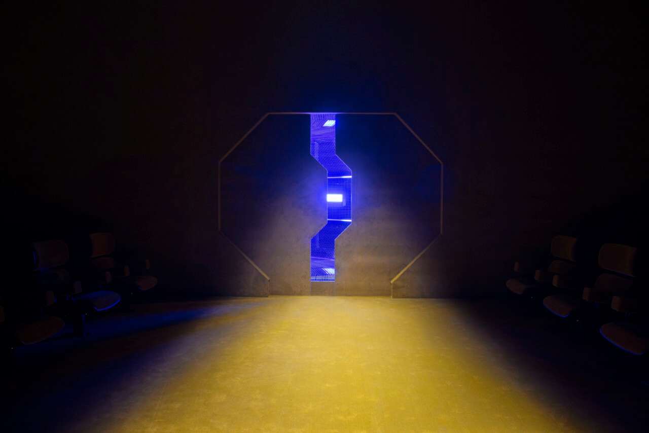 a spaceship-like door opening for the prada 2022 menswear show, letting light onto a yellow carpet