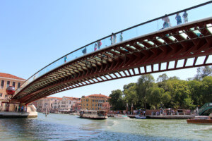 visitors cross a glass-bottomed constitution bridge spanning a canal in venice