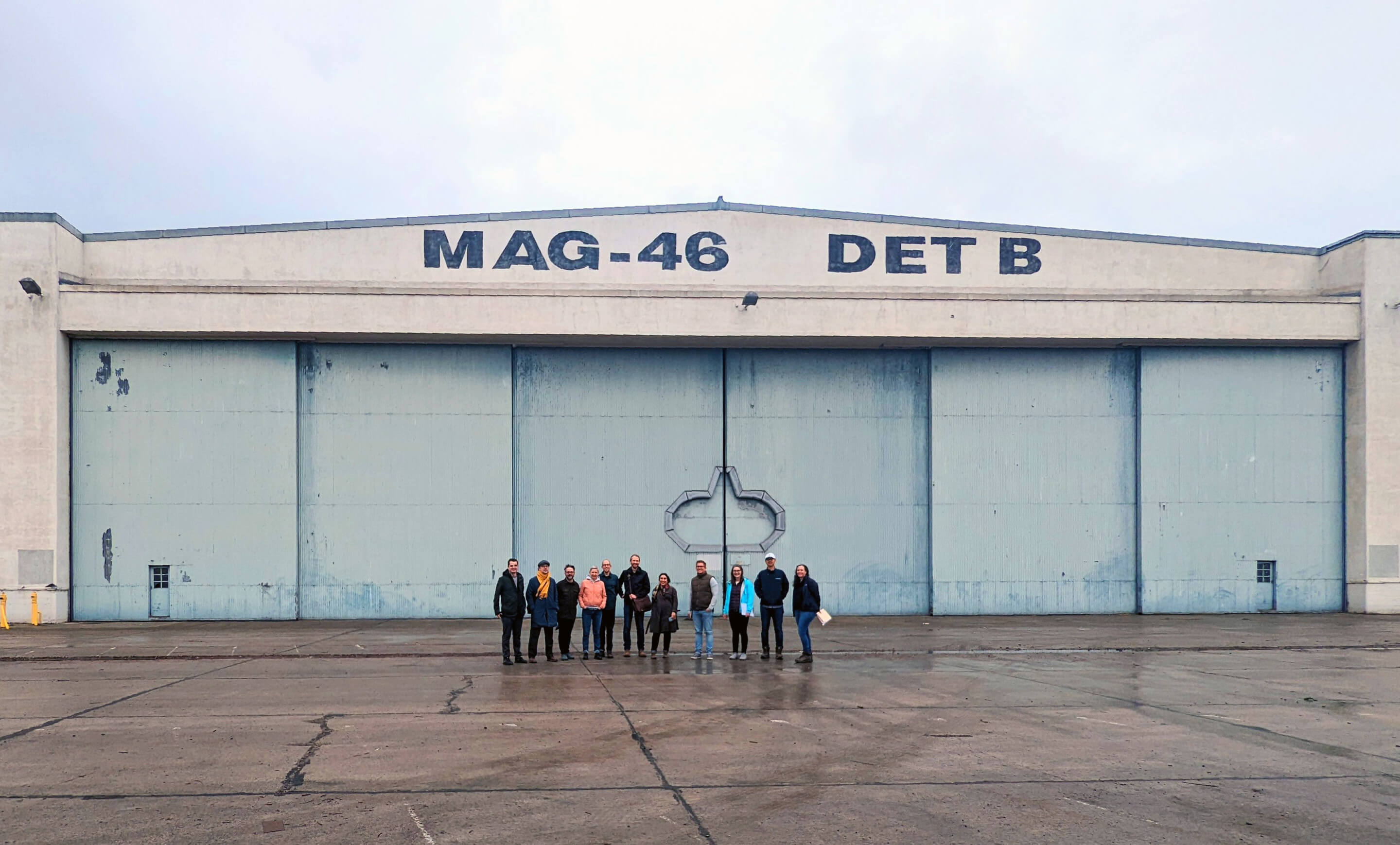 group of people stand in front of an old military aviation hangar