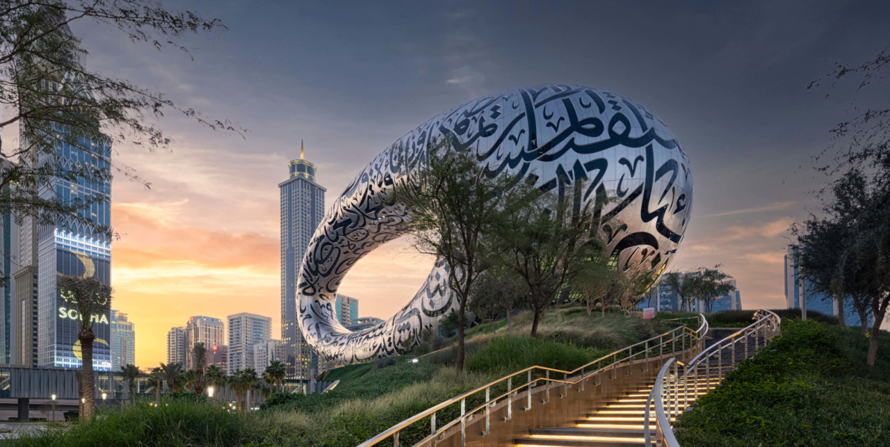 a ring-shaped building atop a grass hill with the dubai skyline in the background, the museum of the future