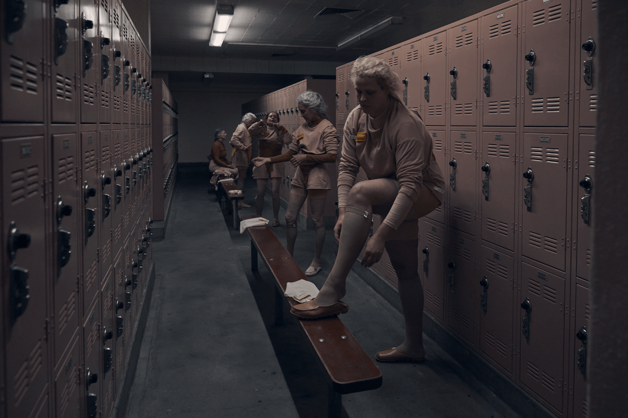 women in a dimly lit gym locker room wearing all beige and matching beige lockers