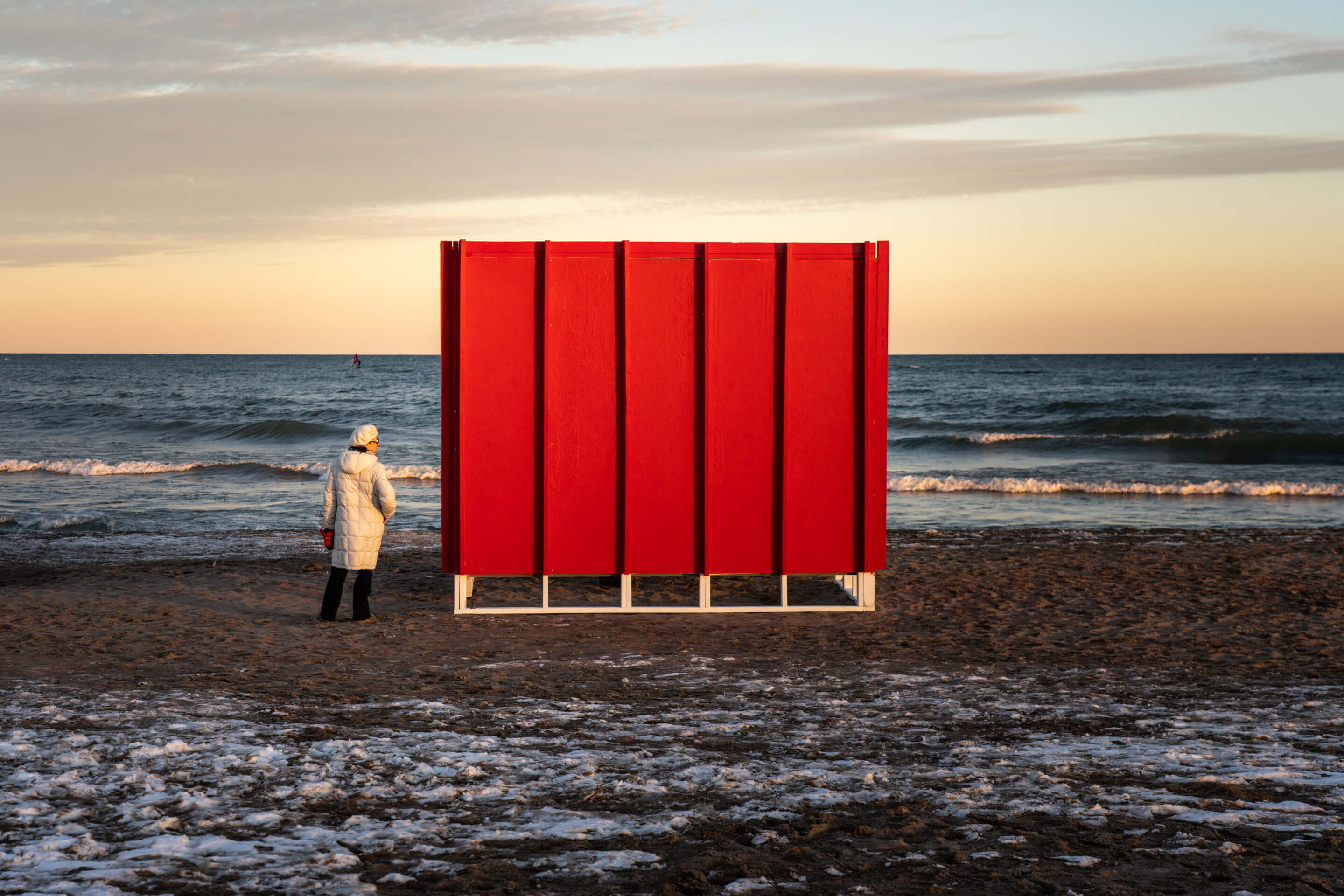 a person approaches a red cube structure on a beach