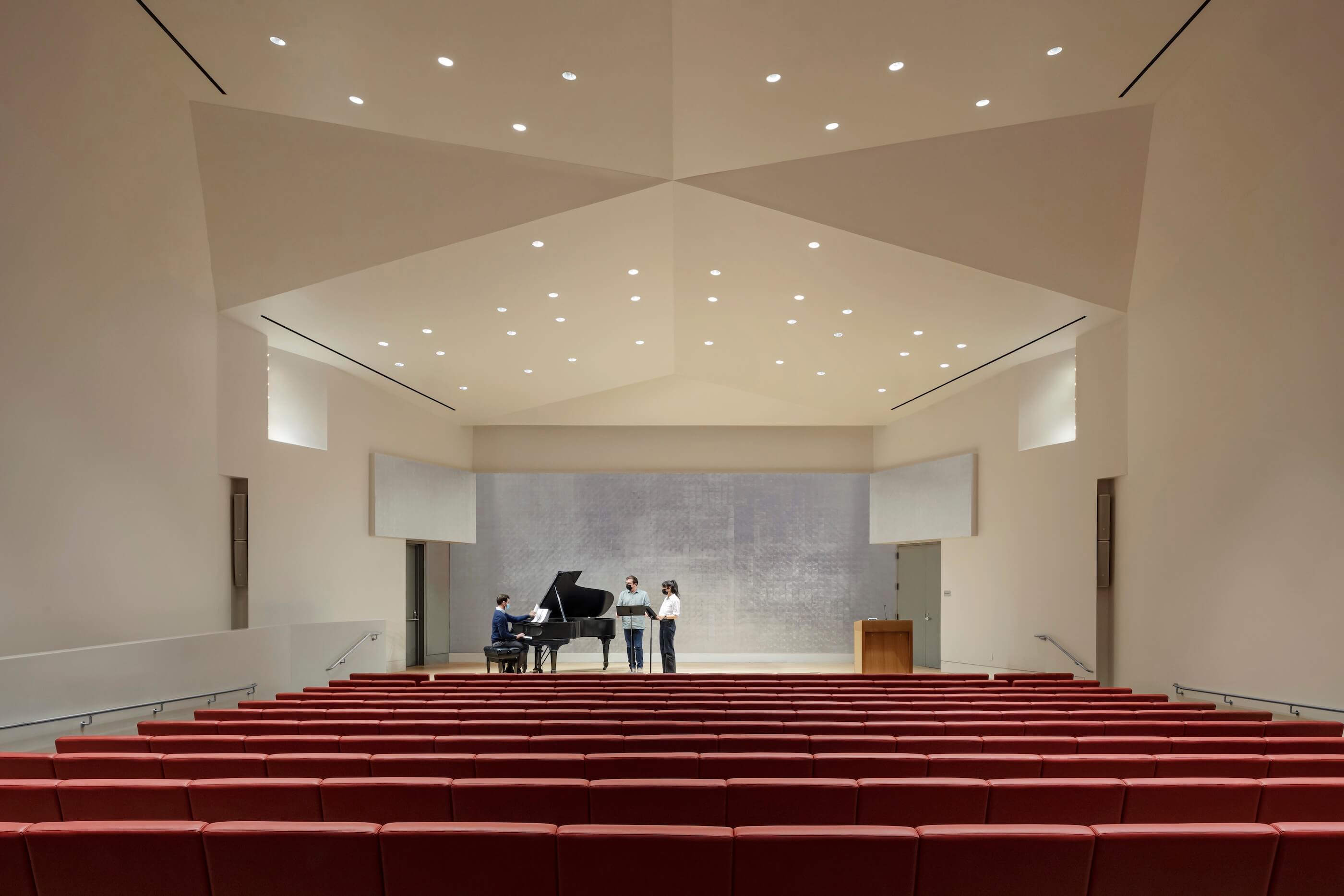 people gather around a piano in a large student auditorium space