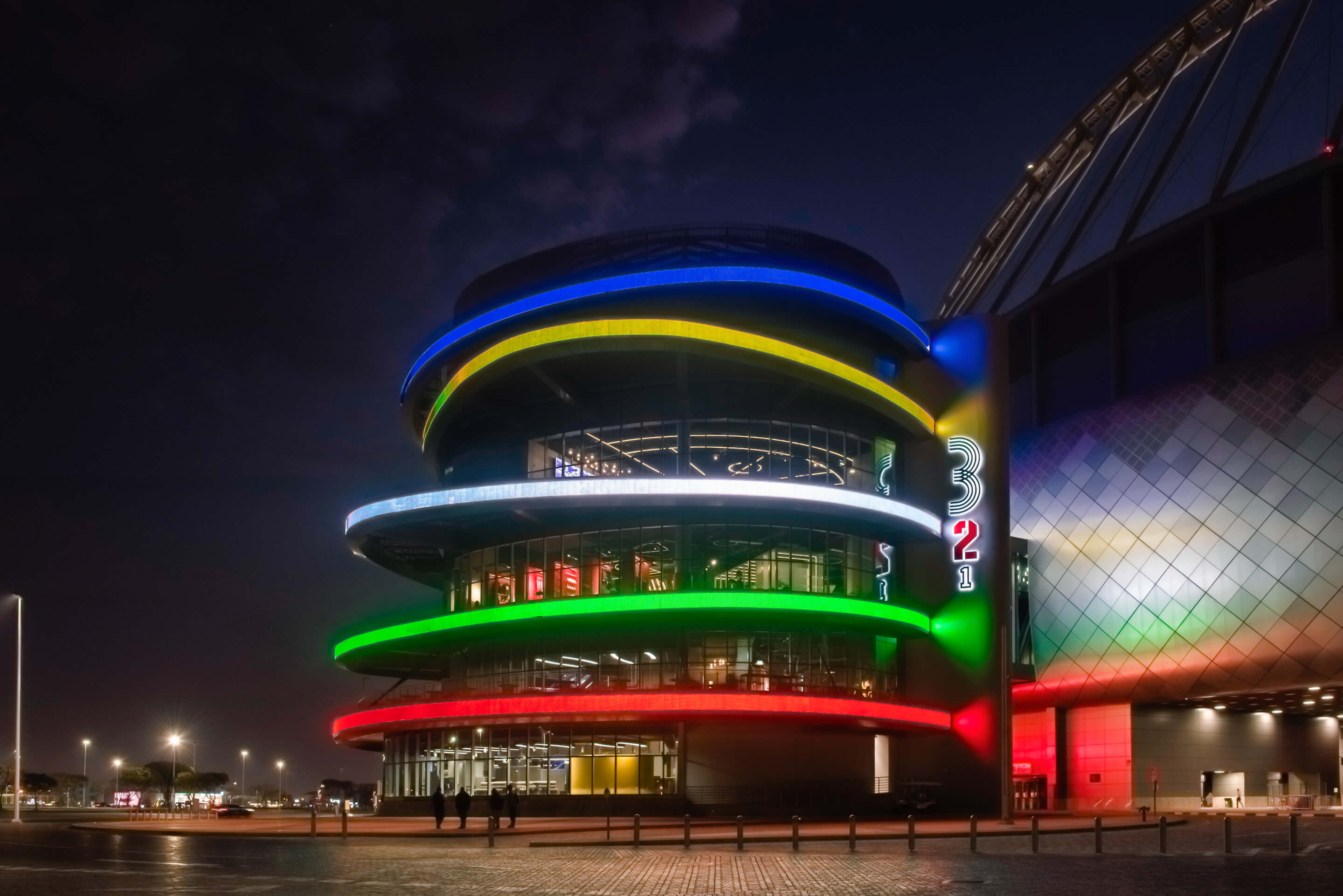 a circular building pictured at night with a facade featuing glowing, Olympic-referencing rings