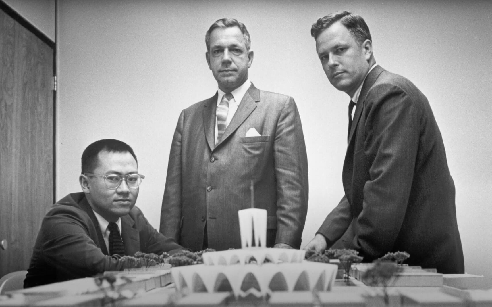 archival photo of three architects posing next to a model