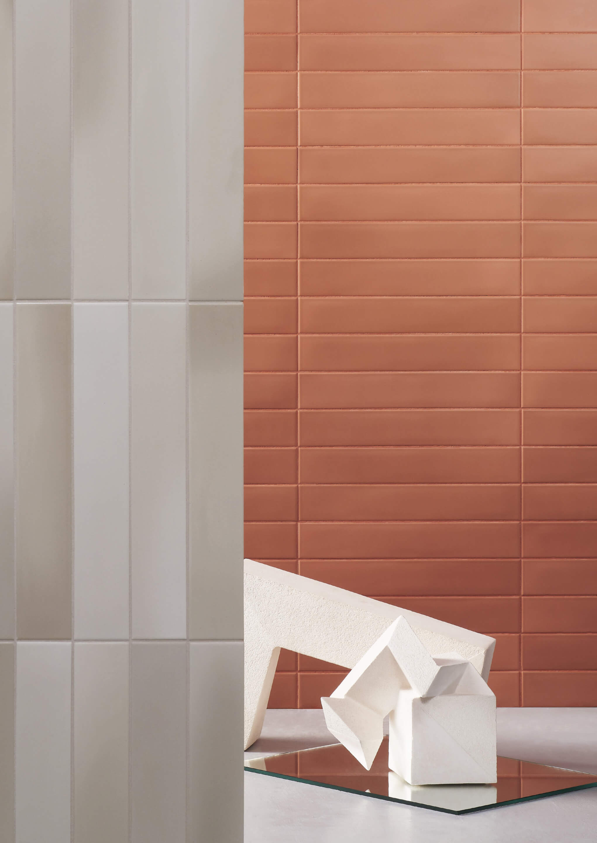 a white sculpture on the floor in front of a wall of terracotta-colored tiles with a wall of vertical dusty white tiles in the foreground occupying left third of the image