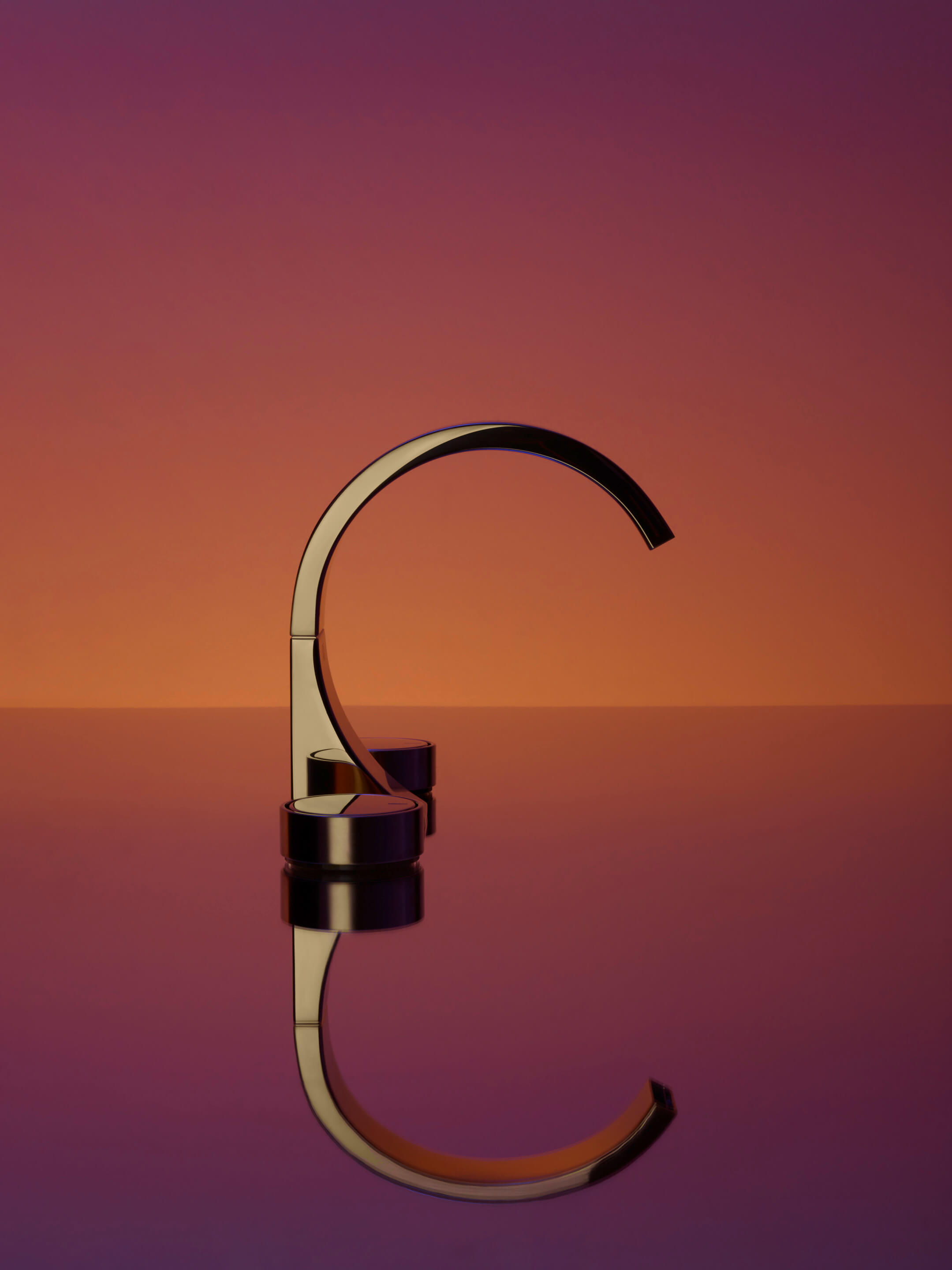 a curved gold faucet in front of an ombre background that fades from purple to orange