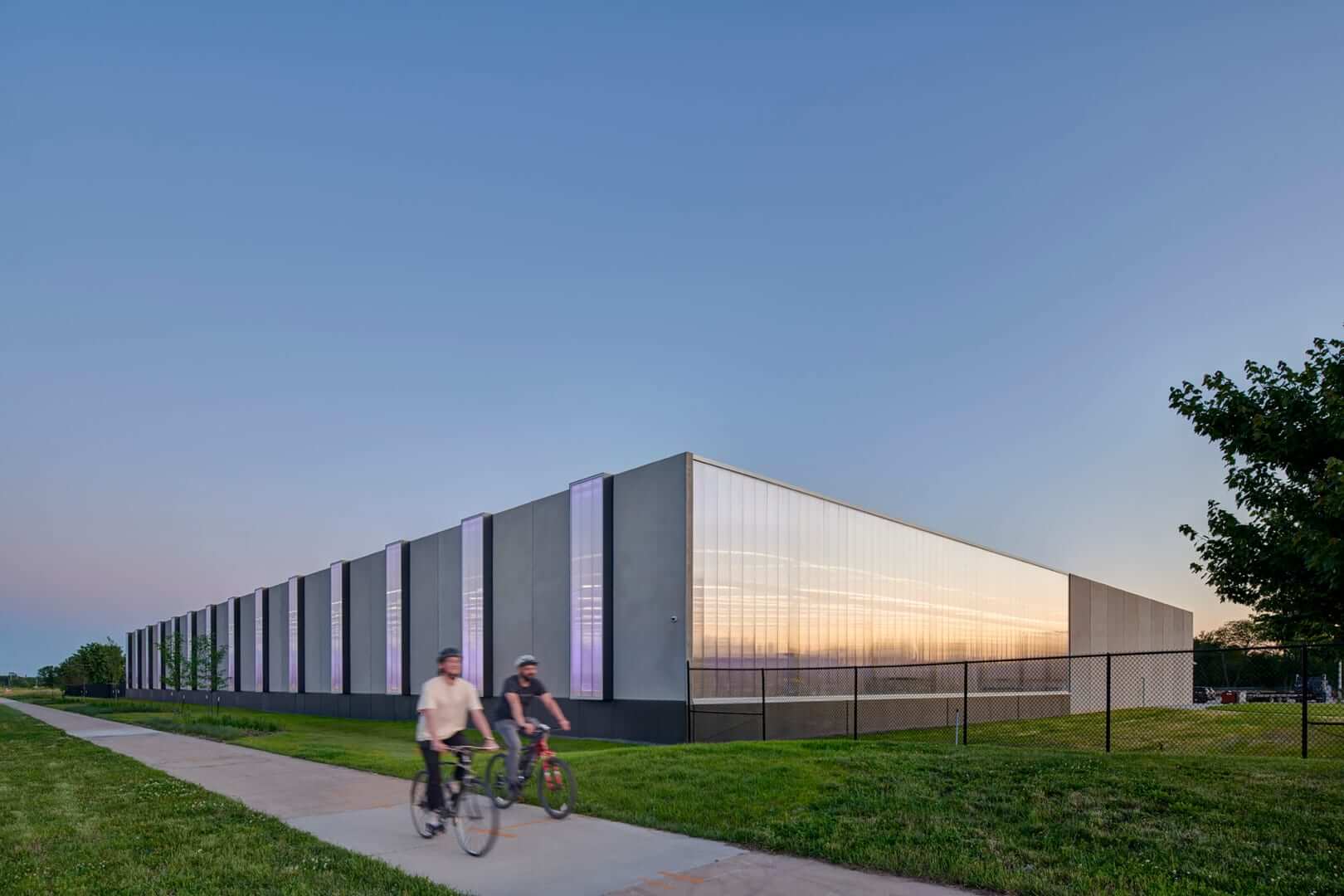 people ride bikes by a long, windowless building