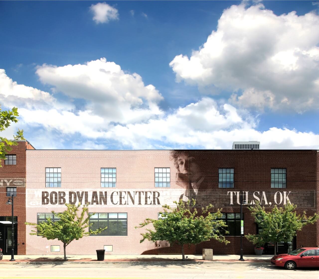 A pale pink building that says "Bob Dylan Center" in black type set against a blue sky with clouds