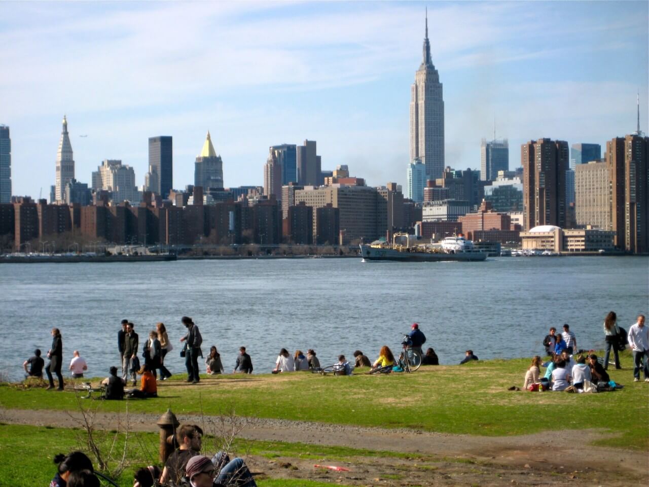 people sitting on a grassy lawn along the east river on a sunny day