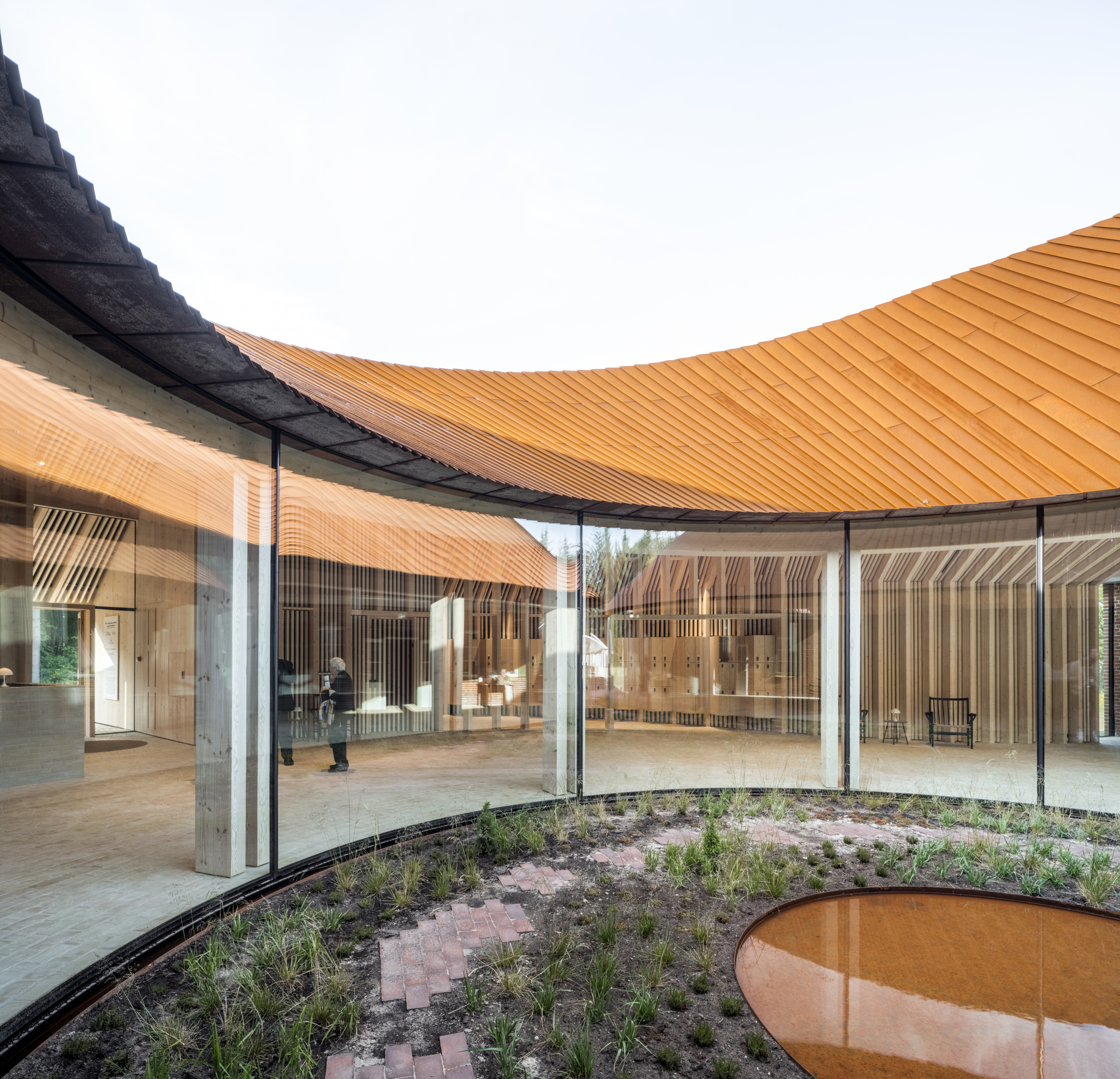 a curving timber structure surrounding a circular courtyard with reflecting pool