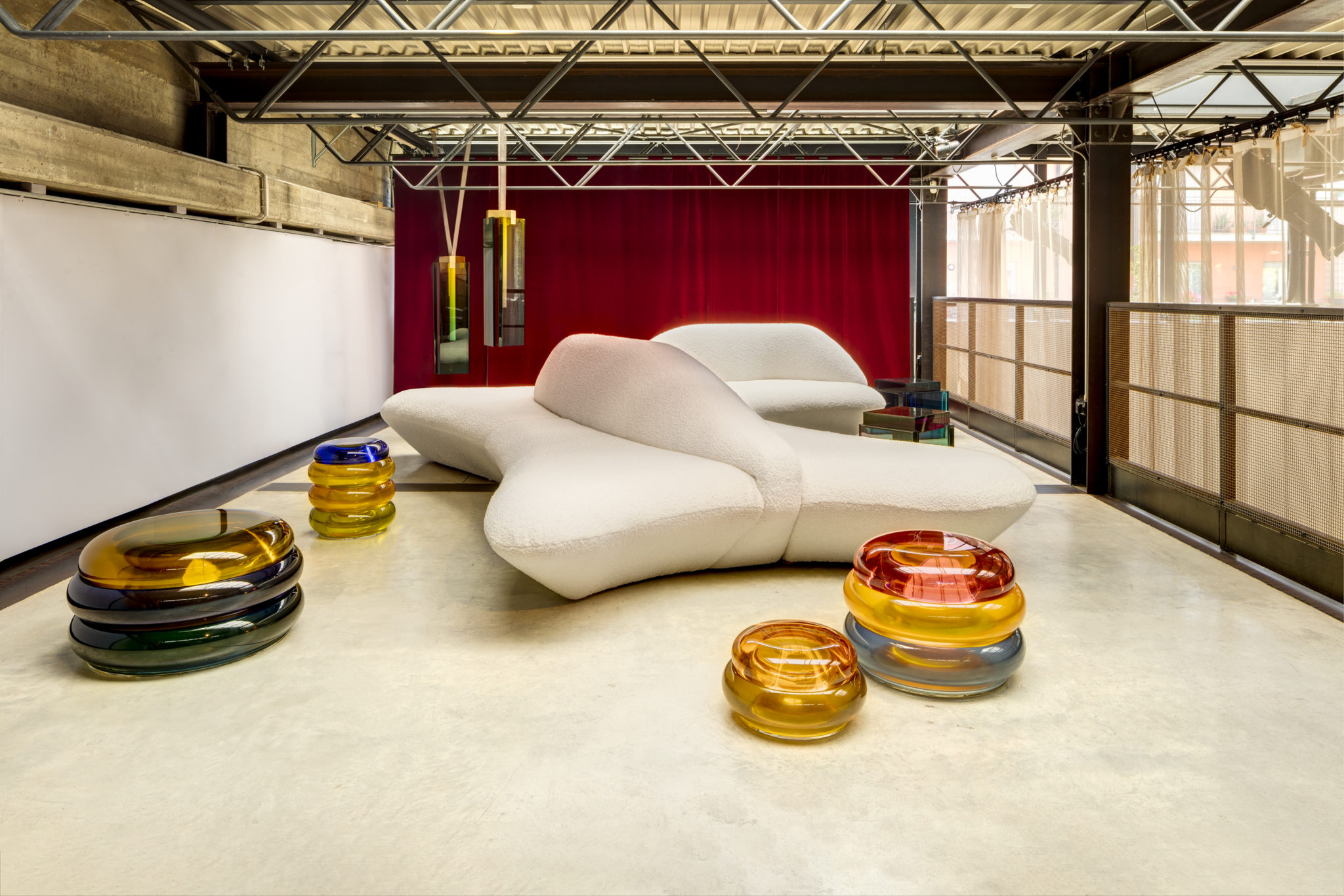 white sofa in front of red curtain surrounded by sculptural pieces