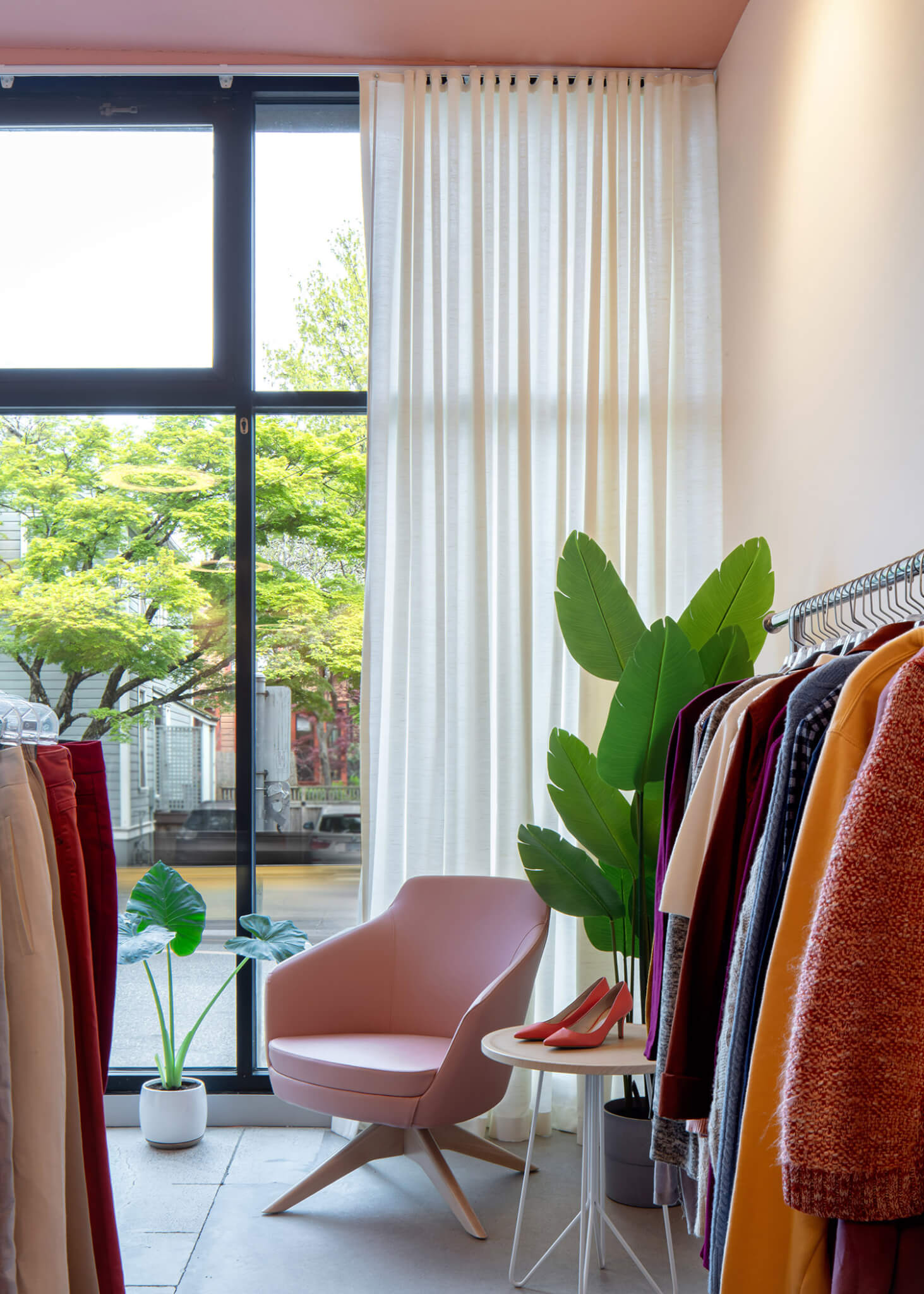 racks of clothing fill a room with a large window and potted plants
