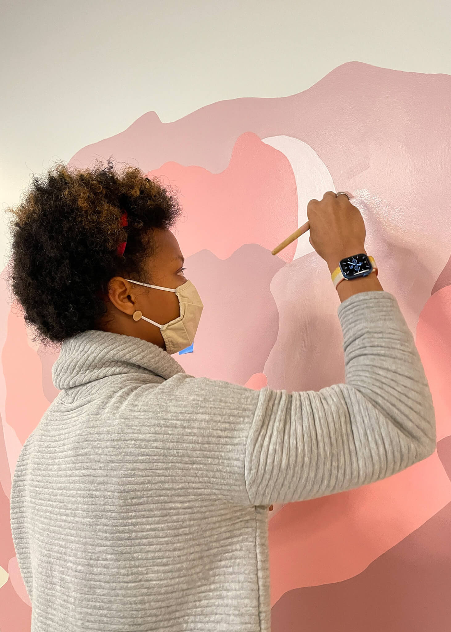 a woman paints a large floral mural in various shades of pink